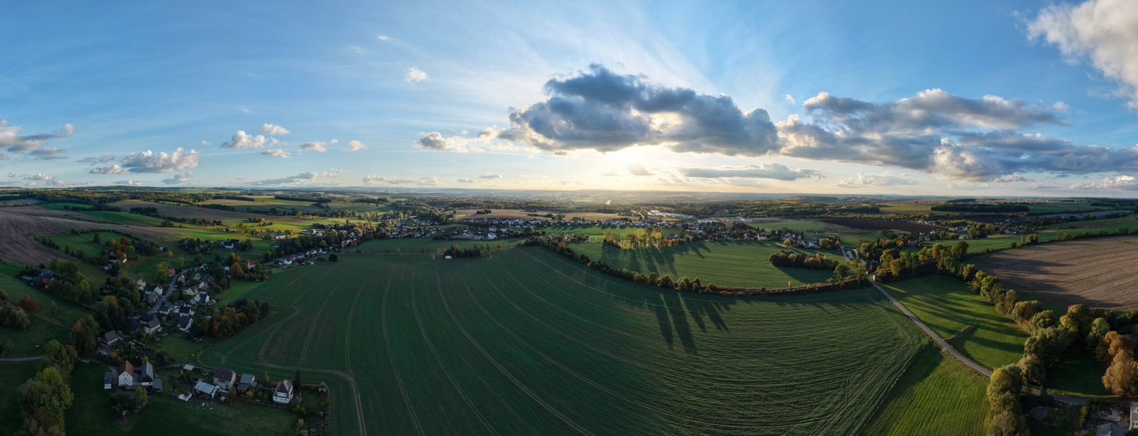 Weitblick über grüne Felder und Dörfer bei Sonnenuntergang, idyllische Landschaft, nachhaltige Landwirtschaft.
