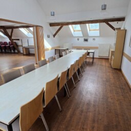 Saal mit einer langen Tafel entlang der Fensterseite